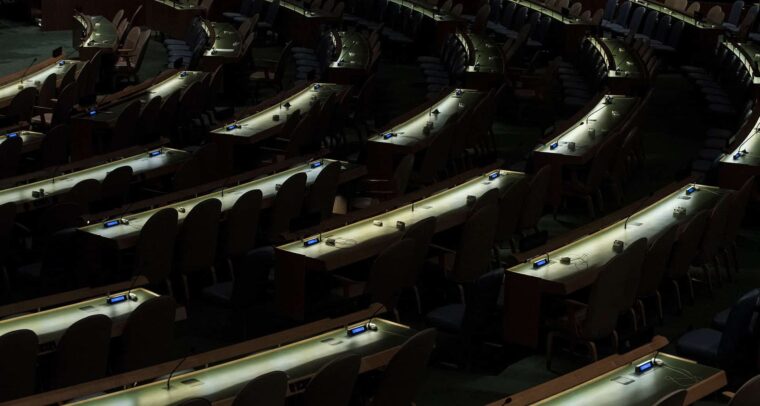 Salón de la Asamblea General de Naciones Unidas después de una reunión, sin delegados presentes, con la única iluminación procedente de los escritorios dispuestos en forma circular. ONU